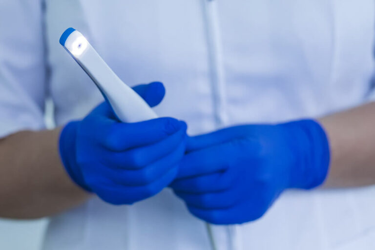 someone holding a intraoral camera with blue latex gloves on