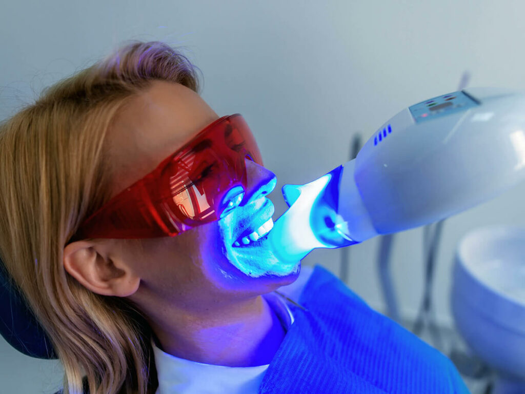 a women wearing protective glasses having her teeth whitened by UV light
