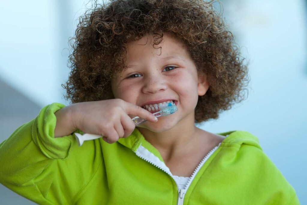 a child smiling while brushing their teeth