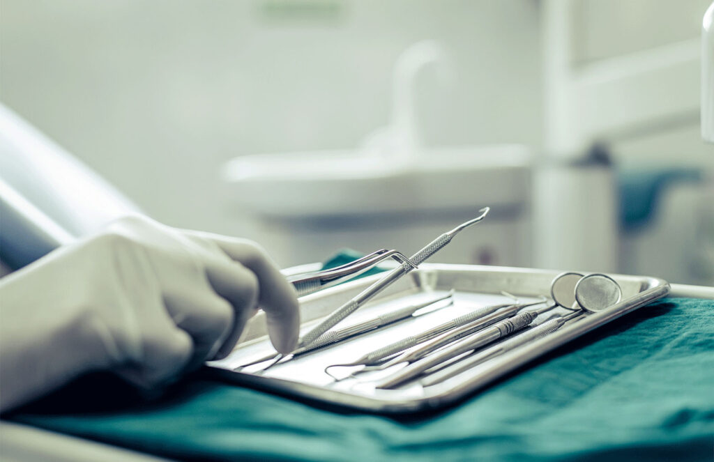 dental tools on a tray with a hand grabbing one of them