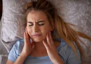 girl holding her jaw in pain while laying on a bed