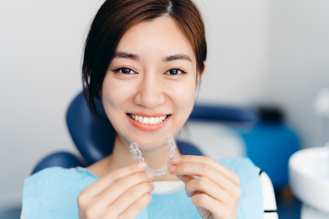 Patient holding clear Invisalign aligners and smiling during orthodontic treatment consultation at Stiles Dental Group.